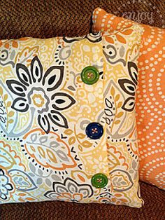 two decorative pillows sitting on top of a couch next to an orange and white pillow