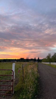 the sun is setting over an open field with a fence and gate in front of it