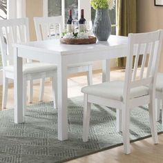 a white dining table with four chairs and a bottle of wine on top of it