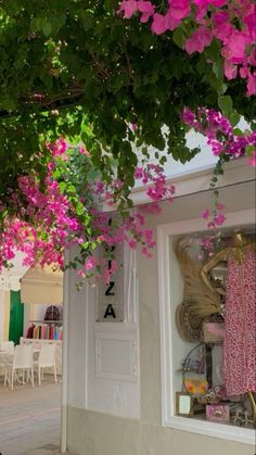 pink flowers are growing on the outside of a storefront in front of tables and chairs