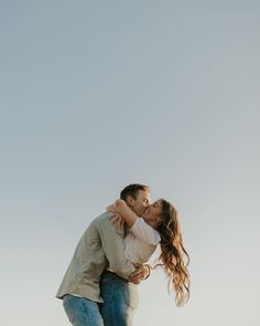 a man and woman kissing while standing on top of a hill with the sky in the background