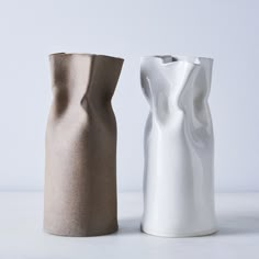 two white and brown vases sitting side by side on a counter top, one is empty