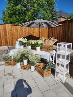 an outdoor table with flowers and plants in containers on the ground next to a wooden fence