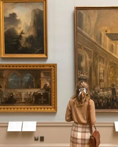 a woman is standing in front of paintings and talking on her cell phone while looking at them