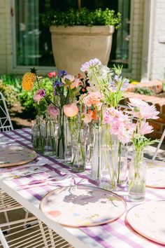 a table topped with vases filled with flowers on top of a purple and white checkered table cloth