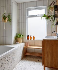 a bath room with a tub a sink and some potted plants on the window sill