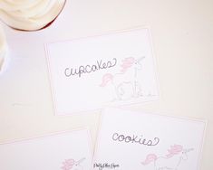 three cards with unicorns on them sitting next to a cupcake and some frosting