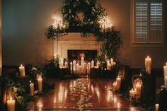 candles are lit in front of a fireplace with greenery on the mantle and around it