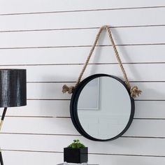 a mirror hanging on the wall next to a table with a lamp and plant in it