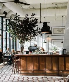 people sitting at tables in a restaurant with plants hanging from the ceiling and large windows