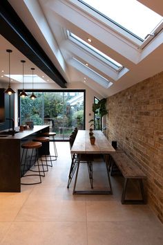 a dining room table and benches in front of an open kitchen area with skylights