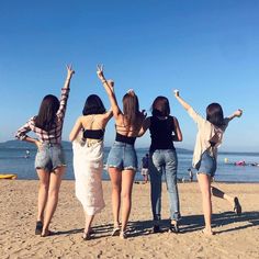 four girls standing on the beach with their arms in the air