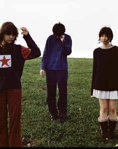 three people standing in the grass with one person covering his face