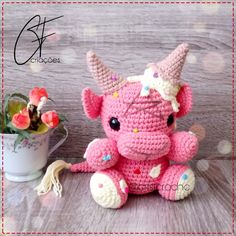 a crocheted pink elephant sitting next to a potted plant