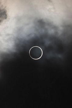 an eclipse in the sky with dark clouds around it and a white circle at the center