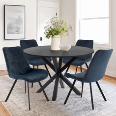 a dining room table with blue chairs and a white vase on top of the table