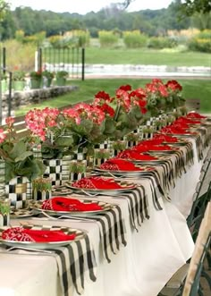 a long table with red plates and flowers on it