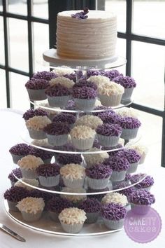 a tiered cake with cupcakes on the top is decorated with purple and white frosting