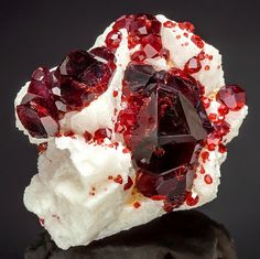 a cluster of red and white crystals sitting on top of a piece of black rock