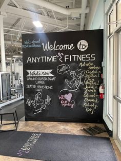 a welcome sign for an anytime and fitness gym with chalk writing on the front wall