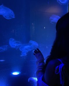 a woman is looking at jellyfish in an aquarium with blue lights on the walls