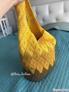 a hand holding a yellow knitted basket on top of a blue bedspread