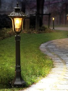 a lamp post sitting on top of a sidewalk next to a light pole in the grass