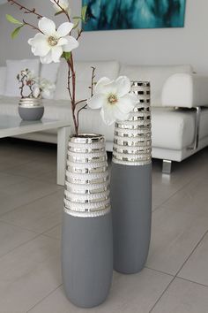 two gray vases with flowers in them on the floor next to a white couch