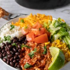 a white bowl filled with mexican food on top of a marble counter next to a fork