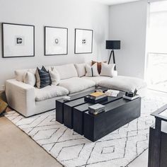 a living room with white couches and black coffee table in front of three framed pictures on the wall