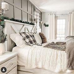 a white bed topped with lots of pillows next to a window covered in christmas decorations