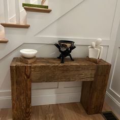 a wooden table sitting under a stair case next to a bowl and vase on top of it