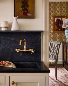 a kitchen sink with gold faucet and black counter top next to a painting on the wall