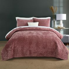 a bed with a pink comforter and two pillows on top of it in a room