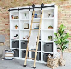 a ladder leaning against a white bookcase in front of a brick wall with baskets and plants