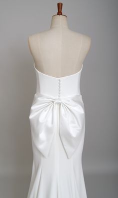 the back of a white wedding dress with a large bow on it's waist