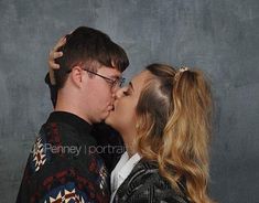 a man and woman kissing each other in front of a gray background