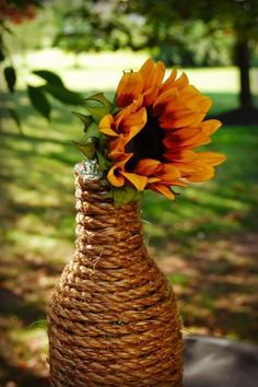 a large sunflower is in a woven vase on a table with grass and trees in the background