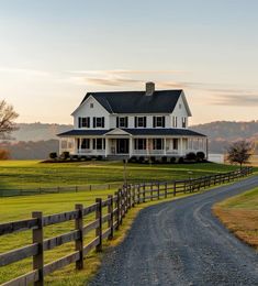 a large white house sitting on top of a lush green field next to a dirt road