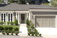 a house with two cars parked in front of it and bushes on the side of the road