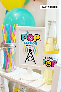 the pop station sign is next to some drinks and straws on a shelf with balloons