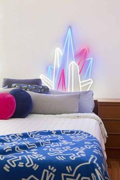 a bed topped with pillows and blankets next to a neon light sign on the wall