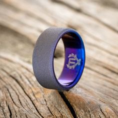 a purple and blue ring sitting on top of a piece of wood with an anchor in the center