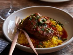 a white bowl filled with rice and meat on top of a wooden table next to a fork