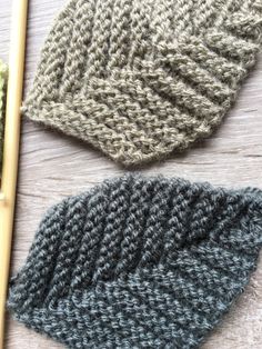 three knitted hats sitting on top of a wooden table next to a knitting needle