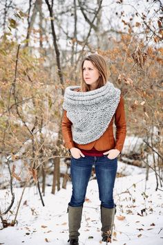 a woman standing in the snow with her hands on her hips, wearing boots and a knitted scarf