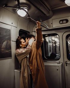 a man and woman kissing while riding on a subway train with their arms around each other