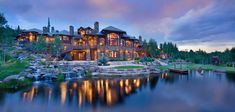 a large house sitting on top of a lush green hillside next to a lake at dusk