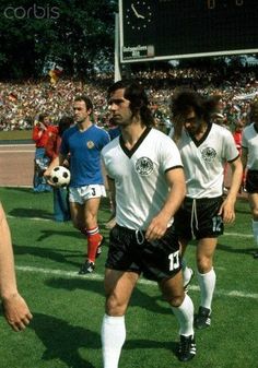 soccer players are walking on the field during a game with spectators in the stands behind them