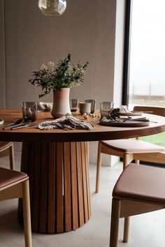 a wooden table topped with a vase filled with flowers next to two chairs and a window